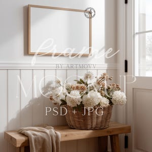 May include: A rectangular wooden frame hangs above a wooden bench with a woven basket filled with white and tan flowers. A beige blanket rests on the bench. The image includes the text "Frame" and "Mockup PSD + JPG".