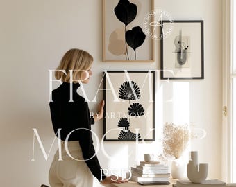 Puede incluir: Tres impresiones artísticas enmarcadas con diseños abstractos en negro y beige cuelgan de una pared blanca. Una persona con una parte superior negra y pantalones crema está cerca de la obra de arte. Un escritorio con libros y decoración está en primer plano. El texto "FRAME BY ARTMOVA" es visible.