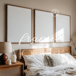 May include: Three framed blank canvases with wooden frames are mounted above a bed with white bedding. A wooden nightstand with a lamp and candles is on the left. The image includes the text "frame by artmovv" and "mockup psd + jpg".