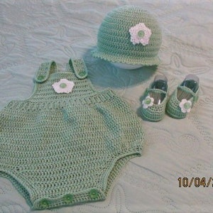 May include: A crocheted baby outfit in a light green color. The outfit includes a hat, a one-piece romper, and a pair of shoes. Each piece has a white flower embellishment.