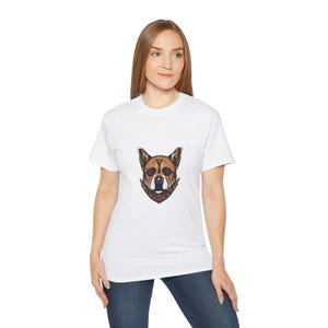 Puede incluir: Una camiseta blanca con un gráfico de cabeza de perro marrón y blanco en la parte delantera. El perro lleva una bandana.