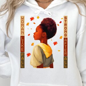 May include: White hoodie with a graphic of a Black girl with brown hair looking up at falling leaves. The text "Woman Like Fall Strong After All" is printed vertically on the hoodie.