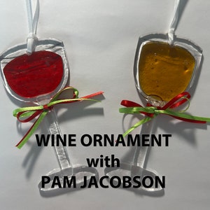 May include: Two glass wine glass ornaments with red and yellow liquid inside. The ornaments are tied with red, green, and white ribbon. The text "WINE ORNAMENT with PAM JACOBSON" is below the ornaments.
