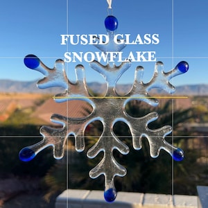 May include: A clear glass snowflake ornament with blue glass accents. The snowflake is fused glass and has a rustic, handmade look. "Fused Glass Snowflake" is written in white text on the image.