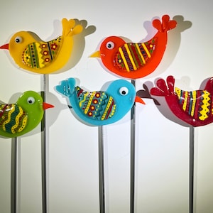 May include: Five colorful glass bird figurines on metal sticks. The birds are decorated with geometric patterns in red, yellow, green, blue, and orange.