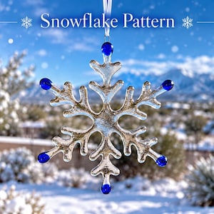 May include: A clear glass snowflake ornament featuring six points, each tipped with a small, round, cobalt blue glass bead. The ornament hangs from a white ribbon and displays the text Snowflake Pattern at the top of the image.