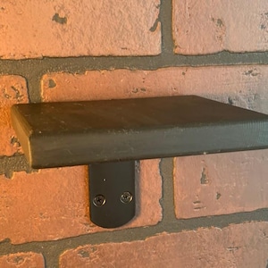 May include: A black wooden shelf with a black metal bracket mounted to a brick wall.