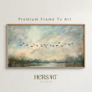 Puede incluir: Pintura de paisaje enmarcada con una bandada de pájaros en vuelo contra un cielo nublado. La obra presenta una paleta de colores apagados de azules, verdes y amarillos. El texto "Premium Frame Tv Art" y "HERSART STUDIO" son visibles.
