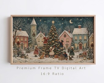 Op de afbeelding: Een ingelijste digitale kunstdruk met een besneeuwd dorpsgezicht bij nacht, waarop kinderen een grote kerstboom versieren. De afbeelding bevat huizen, een klokkentoren, een maansikkel, sterren en de tekst Premium Frame TV Digital Art 16:9 Ratio.