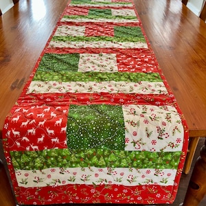 Peut inclure: Un chemin de table matelassé sur le thème de Noël. Il présente un design patchwork avec des tissus rouges, verts et blancs. Les tissus ont différents motifs, notamment des rennes, des cannes en sucre et des flocons de neige.