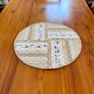 Peut inclure: Un dessous-de-plat rond et matelassé avec un motif patchwork. Le dessous-de-plat présente un fond crème avec des bandes de tissu à motifs floraux et à motifs dans les tons beige, rose et vert. Les bords sont finis avec une bordure coordonnée.