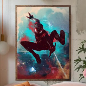 May include: Framed artwork featuring a dynamic illustration of a superhero in a black and red suit, mid-air. The background showcases a cityscape with vibrant blue, red, and orange hues, creating a dramatic and action-packed scene.