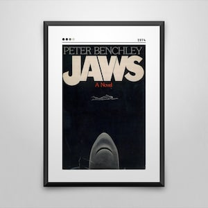 May include: Framed poster of the book cover for "Jaws" by Peter Benchley. The poster features the title in large, off-white letters against a black background, with a shark's open mouth at the bottom and a swimmer above.