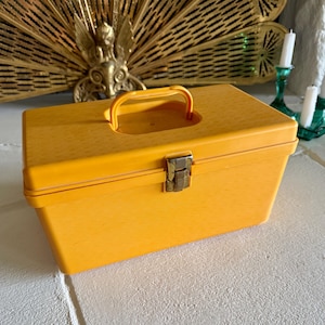 May include: A rectangular yellow plastic storage box with a smooth finish and a wood grain texture. The box features a top-mounted handle and a single metallic silver-toned latch on the front centre to secure the lid in a closed position.