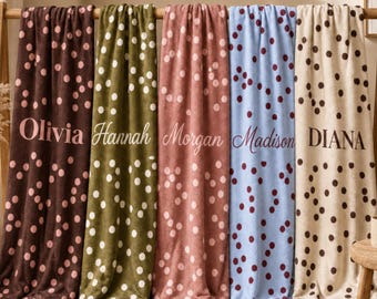May include: Five soft blankets hanging on a wooden rack, each featuring a unique color and polka dot pattern. The blankets are personalized with the names Olivia, Hannah, Morgan, Madison, and Diana printed in various fonts across the center.
