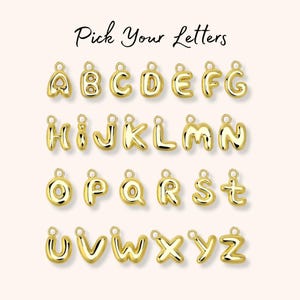 May include: A collection of gold-toned, three-dimensional, puffy-style alphabet letter charms, each featuring a small circular jump ring at the top for attachment. The text "Pick Your Letters" is displayed in a black script font above the charms.