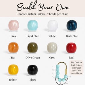May include: A collection of ten round beads in pink, light blue, white, dark blue, tan, olive green, grey, red, yellow, and black. A gold-toned oval carabiner chain features seven light blue beads arranged in a numbered sequence from one to seven.