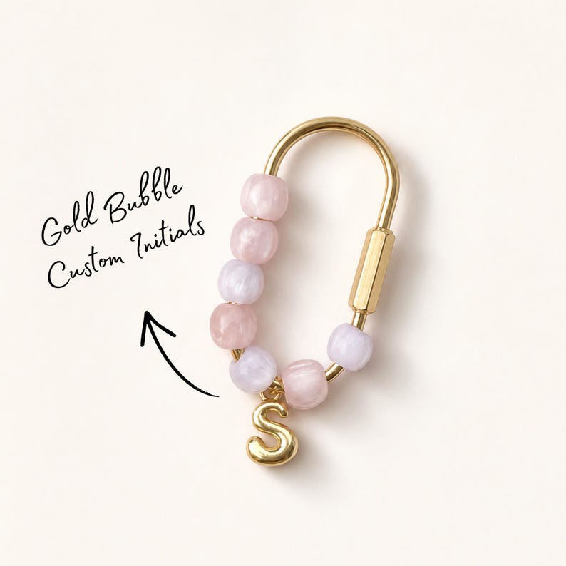 May include: A gold-toned metal carabiner keychain featuring a series of light pink and lavender translucent bubble beads threaded along one side, with a gold-toned letter S charm hanging from the bottom. Text reads Gold Bubble Custom Initials.