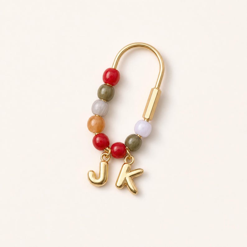 May include: A gold-toned U-shaped charm holder featuring a series of colorful beads in shades of red, olive green, orange, and light purple. Two gold-toned letter charms, J and K, are suspended from the bottom of the beaded U-shaped metal frame.