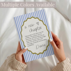May include: A rectangular notebook with a light blue and white vertical striped cover. A central scalloped gold frame contains the text: a new chapter, followed by an inspirational quote and the name Diana in a black cursive script font.