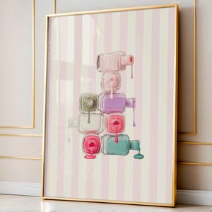 May include: A framed art print featuring a stack of nail polish bottles in various pastel colors, with dripping polish. The background has vertical pink and white stripes. The frame is gold.