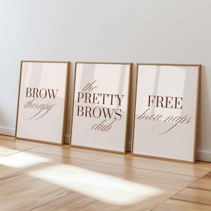 May include: Three framed wall art prints with light backgrounds and dark brown text. The first print reads BROW therapy, the second reads the PRETTY BROWS club, and the third reads FREE brow naps. Each print is encased in a thin light wood frame.