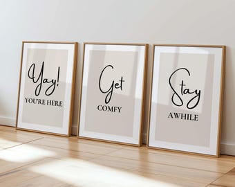 May include: Three framed art prints with a neutral color palette. Each print has a beige background with black text. The first print says "Yay! You're Here", the second says "Get Comfy", and the third says "Stay Awhile".