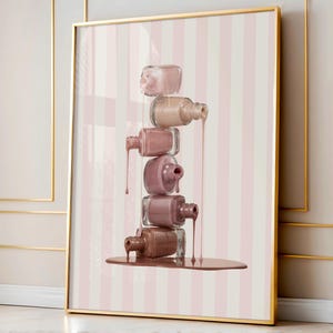 May include: A framed print featuring a stack of nail polish bottles in various shades of pink and brown. The bottles are arranged to appear as if the polish is dripping down, creating a visually appealing effect. The background has pink and white vertical stripes.