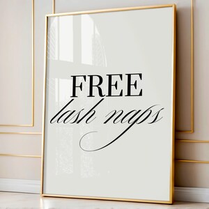 Puede incluir: Una impresión enmarcada con un marco dorado. La impresión tiene un fondo blanco con las palabras "FREE" en negrita, en negro, sobre las palabras "lash naps" en cursiva, en negro.