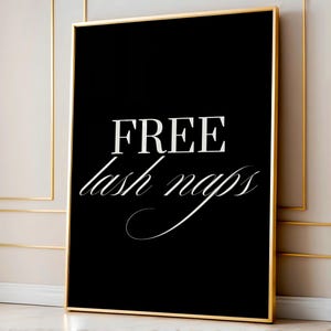 Puede incluir: Una impresión enmarcada en blanco y negro con las palabras "FREE lash naps" en tipografía elegante. El texto es blanco sobre un fondo negro, enmarcado en un borde dorado. La impresión se muestra contra una pared neutra.