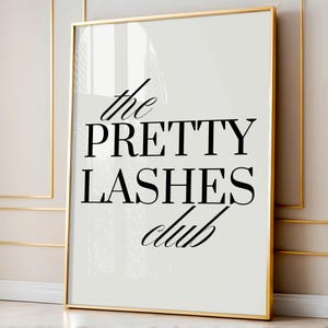 May include: A framed print with the words "the PRETTY LASHES club" in black script and block letters. The print has a white background and a gold frame. The image is displayed against a neutral wall.