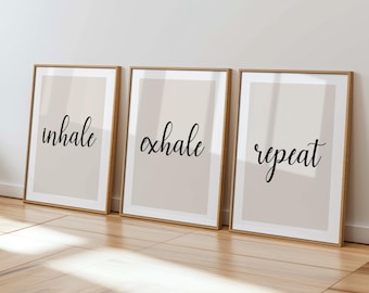 Puede incluir: Tres impresiones artísticas enmarcadas con las palabras "inhale", "exhale" y "repeat" en elegante escritura negra. Las impresiones tienen un fondo beige neutro y están enmarcadas en dorado, creando una estética minimalista.