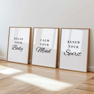 Puede incluir: Tres impresiones artísticas enmarcadas con texto inspirador. Las impresiones tienen un fondo blanco con texto negro que dice "Relax Your Body", "Calm Your Mind" y "Renew Your Spirit". Los marcos son de color marrón claro.