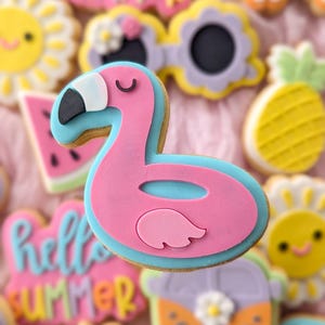 May include: A pink and blue flamingo cookie with closed eyes. The cookie is decorated with white icing and is surrounded by other summer-themed cookies, including a watermelon slice, a sun, and a van.