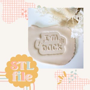 May include: A beige clay imprint of a white snowflake and the text "I'm back" in a white cloud shape. The imprint is on a beige surface. The text "STL file" is in a colorful circle in the lower left corner of the image.