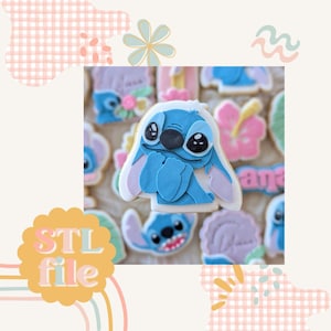 May include: A blue and white cookie decorated with a cartoon character resembling Stitch from the Disney movie Lilo & Stitch. The cookie is surrounded by other cookies with various designs, including flowers and a hibiscus.