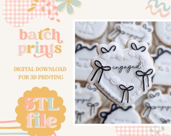 May include: White heart-shaped cookie decorated with black bows and the word "engaged" in black script. The cookie is surrounded by other similar cookies. The image also includes the text "batch prints" and "STL file".