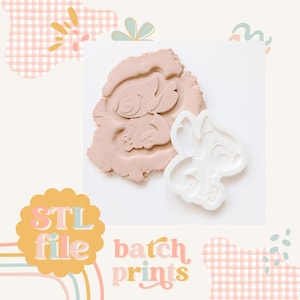 Pode incluir: Um cortador de biscoitos impresso em 3D branco em forma de Stitch de Lilo & Stitch. O cortador é mostrado pressionado em uma argila rosa claro. O texto "STL file batch prints" é visível na imagem.