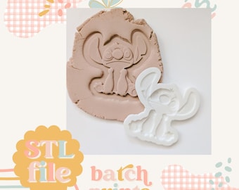 May include: White plastic cookie cutter in the shape of Stitch from Lilo & Stitch. The cutter is shown pressed into a brown clay surface, leaving an impression of the character.