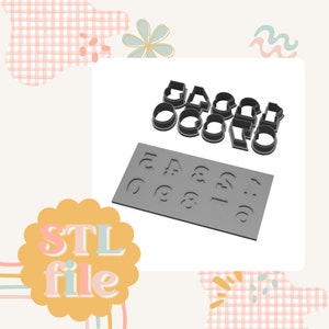 May include: A set of 3D printed cookie cutters in the shape of letters and numbers. The cutters are grey and are arranged on a grey surface. The letters and numbers are in a font that is similar to a children's font. The cutters are designed to be used with fondant or cookie dough.