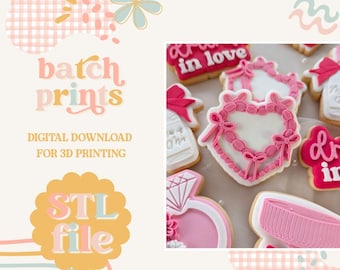 May include: Image features decorated cookies with pink and white icing in various shapes, including a heart, ring, and gift. The cookies are arranged on a light-colored surface. The image also includes text that says "batch prints" and "STL file".