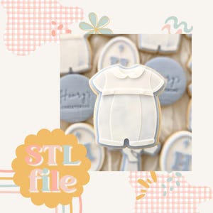 May include: A white cookie decorated with a baby onesie design. The cookie is surrounded by other cookies with various designs, including a blue cookie with the word "Happy" on it.