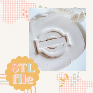 Könnte beinhalten: Eine weiße 3D-gedruckte Form zum Herstellen eines Charms aus Harz oder Polymer Clay. Die Form ist kreisförmig mit einem horizontalen Balken in der Mitte. Die Form liegt auf einer weißen Oberfläche. STL-Datei.