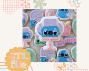 May include: A blue and purple cookie decorated with a Stitch character from the Disney movie Lilo & Stitch. The cookie is shaped like a pedestal and has a pink base. The cookie is surrounded by other cookies with various designs.