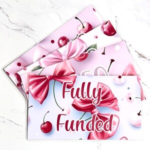 May include: A set of three clear plastic budget envelopes with a pink cherry and bow design. The front envelope has the words "Fully Funded" in white script. The envelopes are arranged in a fan shape.