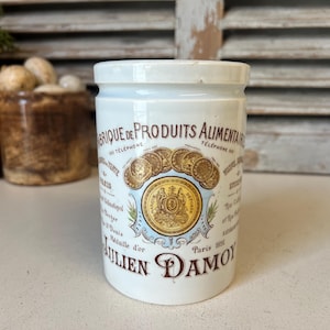 Puede incluir: Tarro de cerámica blanca con una etiqueta azul y dorada que dice "Fabrique de Produits Alimentaires - Teléfono 155 - París - Julien Damoy". La etiqueta presenta un escudo con una corona y una pancarta que dice "París 1891".
