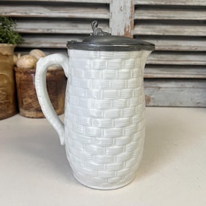 May include: White ceramic jug with a woven pattern and a pewter lid. The jug has a handle and a spout.