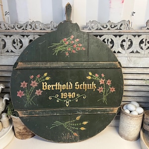 May include: A round, green wooden sign with painted flowers and the text "Berthold Schuk 1940".