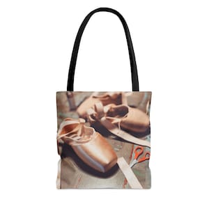 Puede incluir: Una bolsa de tela con un diseño de zapatillas de ballet, cintas y tijeras sobre una superficie de madera.
