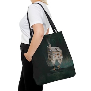 May include: A black tote bag with a dark green design featuring a small house with a chimney on top of a pair of chicken legs.